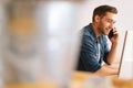 Side view of focused young business man talking on mobile phone sitting at desk with monitor computer at home office. Royalty Free Stock Photo