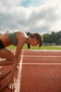 Side view of focused young female runner getting ready to start race on track field in the daytime Royalty Free Stock Photo