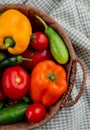 side view of fresh vegetables ripe tomatoes colorful bell peppers green chili peppers and cucumbers in a wicker basket on plaid Royalty Free Stock Photo