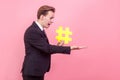 Side view of frustrated shocked man holding big hashtag symbol and looking in surprise. indoor, studio shot, pink background