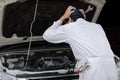 Side view of frustrated stressed young mechanic man in white uniform touching his head with hands against car in open hood at the Royalty Free Stock Photo