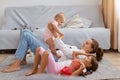 Side view full length portrait of smiling woman holding baby daughter in hands while lying on floor, mother playing with her Royalty Free Stock Photo