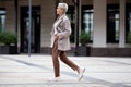 Side view full length woman walks outside and wears trendy business clothes, oversize jacket, tie, pants and white