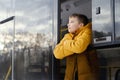 Little boy in orange jacket leaning on open bus window looking up winter sky. Royalty Free Stock Photo