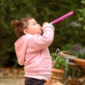 Side view of funny little girl celebrating, blowing in pipes. Birthday outdoor party, Purim.