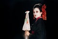 View of geisha in black kimono with red flowers in hair holding traditional asian umbrella isolated on black Royalty Free Stock Photo