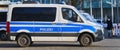 Side view of a German police car, a Mercedes-Benz blue and white painted van, parked on the pavement and manned by police officers