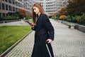 Side view of gorgeous stylish girl walking around street with cellphone and suitcase