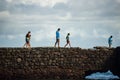 Side view of a group of people walking on the breakwater of Porto da Barra beach against cloudy sky