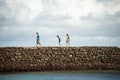 Side view of a group of people walking on the breakwater of Porto da Barra beach against cloudy sky