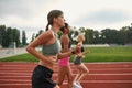 Side view of group of three professional young female runners running together on track field at the stadium Royalty Free Stock Photo