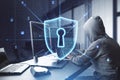 Side view of hacker at desktop using computers with creative glowing web security shield on blurry office interior background. Royalty Free Stock Photo