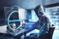 Side view of hacker in hoodie using computers on desktop with creative polygonal blockchain hologram on blurry interior background