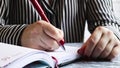 Side view of the hands of a woman with red nails, holding a red pen, writes something on an empty sheet of diary paper lying on a Royalty Free Stock Photo