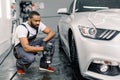 Side view of handsome African American male car wash worker hodling in hand special chemical cleaner solution and Royalty Free Stock Photo