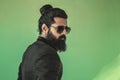 Side view of handsome bearded man from the back with a man bun hairstyle posing in studio wearing a suit and sunglasses on green Royalty Free Stock Photo