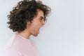 Side view of handsome crazy male with curly hair opens mouth widely, screams loud with hands on mouth, posing on white studio wall