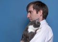 Side view of handsome man in pink shirt holding adorable grey cat on sholder