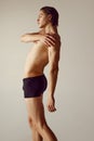 Side view. Handsome shirtless young guy with muscular body standing in underwear against grey studio background. Fitness Royalty Free Stock Photo