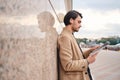 Side view of handsome stylish man in beige coat reading newspaper outdoor