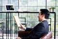 Side view of a happy Asian businessman smiling and reading the newspaper in the morning while sitting on the sofa in the office Royalty Free Stock Photo