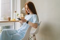 Side view of happy cute young woman in casual clothing using mobile phone sitting at desk by window in cozy light cafe. Royalty Free Stock Photo