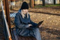 Side view of a happy girl in a coat sitting on a Park bench and using a laptop. The concept of communication. Royalty Free Stock Photo