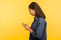 Side view of happy girl in stylish denim shirt typing message and smiling, dialing number calling on cell phone Royalty Free Stock Photo