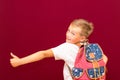 Side view Happy joyful schoolboy wearing backpack and giving thumbs up isolated on red wall Royalty Free Stock Photo