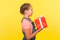 Side view of happy little girl with braid holding gift box and smiling to camera, child enjoying big birthday present Royalty Free Stock Photo