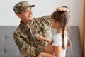 Side view of happy positive smiling soldier man in camouflage sitting with his daughter on sofa, looking how his kid grown when he Royalty Free Stock Photo