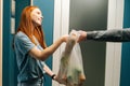 Side view of happy pretty young woman customer receiving groceries bag from unrecognizable delivery man on doorstep at Royalty Free Stock Photo