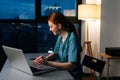 Side view of happy smiling redhead young female doctor in blue green medical uniform working typing on laptop computer. Royalty Free Stock Photo