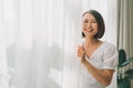 Side view of a happy woman opening curtains of a window and enjoying a new day with a warm light from outdoors Royalty Free Stock Photo