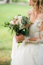 Side view of happy young bride in a beautiful dress holds a bouquet of flowers, outside. Wedding details. Close up