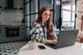 Side view of happy young woman typing on laptop computer sitting at table with coffee cup smiling looking to screen in Royalty Free Stock Photo