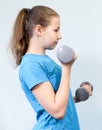 Side view at a healthy teen age fitness girl doing exercises with two dumbbells, grey background