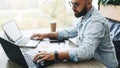 Side view. Hipster bearded businessman sits in cafe, works on two laptops. Freelancer work remotely. Online education