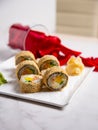 Side view of hot tempura sushi roll with salmon. Red rose petals near served dish on marble background. Sushi roll portion on