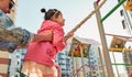 Side view image of active cute little girl climbing on a rope at playground. Mother helping her daughter to climb on a wall with a Royalty Free Stock Photo