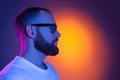 Close up portrait of young caucasian bearded man in sunglasses isolated on dark studio background in neon lights. Side Royalty Free Stock Photo