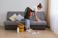 Side view image of young woman cleaning her home, wearing jeans and brown apron, housewife doing her household chores at home in Royalty Free Stock Photo