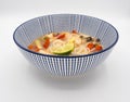 Side view of Japanese ramen noodle soup with shrimps, mushrooms, tomatoes, lemongrass and lime in a blue and white bowl on a white