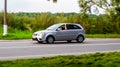 Side view KIA Rio car second generation moving on rural asphalt road. Driver with passenger in old silver color hatchback riding