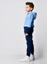 Kid in warm overalls, white sneakers walking along the studio wall. Full-length portrait. Children's fashion, casual Royalty Free Stock Photo