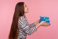 Side view of kind generous woman in striped sweatshirt smiling joyful and giving birthday gift to camera