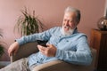 Side view of laughing gray-haired aged male holding cellphone using mobile online app, cheerful looking to screen Royalty Free Stock Photo