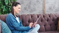 Side view laughing teenage young girl using tablet pc sitting on couch at cosiness living room