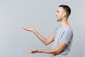 Side view of laughing young man in casual clothes pointing hands aside, holding something isolated on grey wall Royalty Free Stock Photo