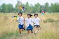 Side view of little Asian girls hold small windmill and look fun to run together in walkway of rice field